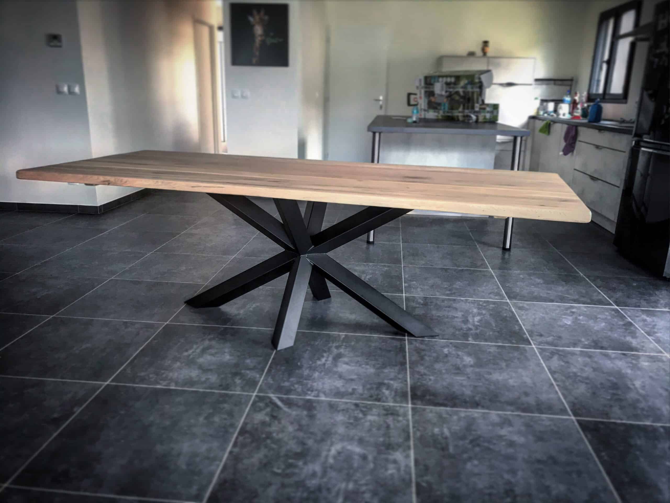 Une table avec un plateau en chêne clair et un pied central Etoile en acier cuit dans une salle à manger avec un carrelage gris foncé