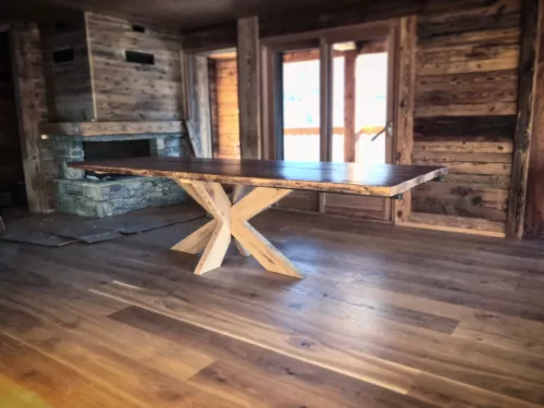 Un salon d'un chalet tout en bois, avec une cheminée en pierre, et une table tout en bois, avec pied de table central en chêne massif